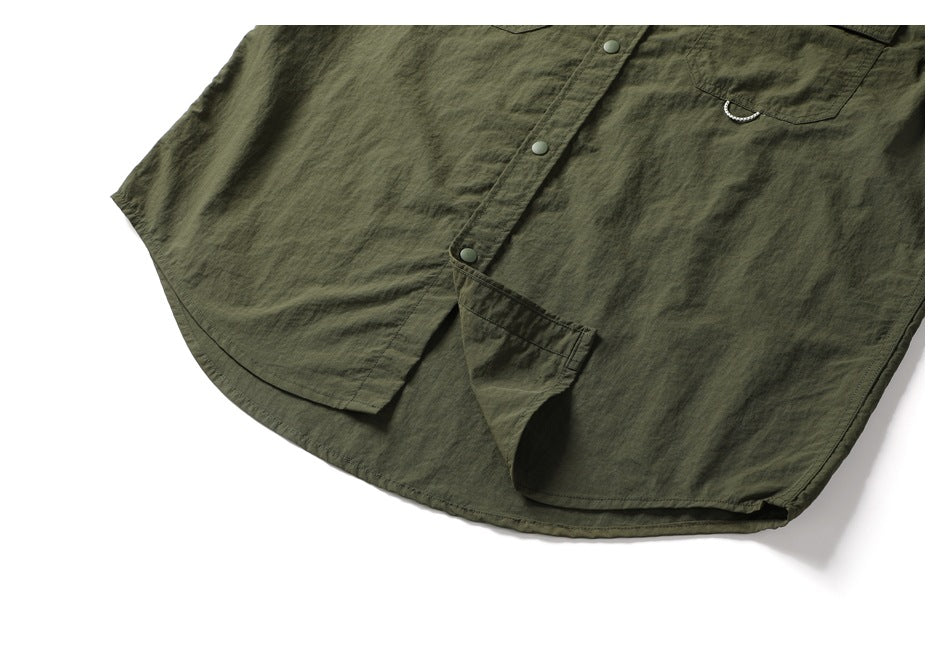 Close-up of an olive-green button-front shirt with a chest pocket, curved hem, and a small metal loop.