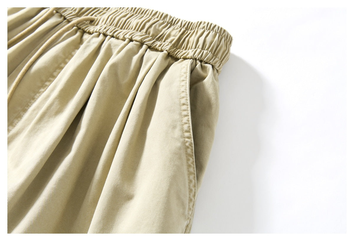 Close-up of beige trousers showing the elastic waistband, front pleats and angled side pocket.