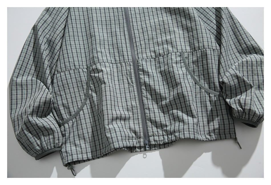Cropped flat lay of a gray-green plaid hooded jacket front with a center zipper, curved pockets, elastic cuffs, and drawcord