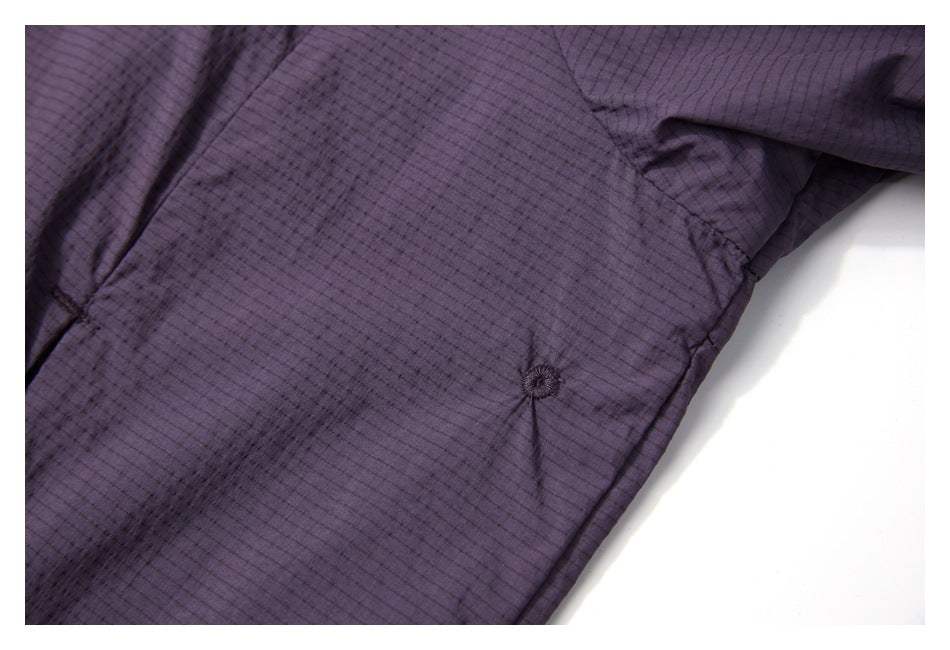 Close-up of dark purple jacket fabric, a stitched seam, and a small circular stitched feature.