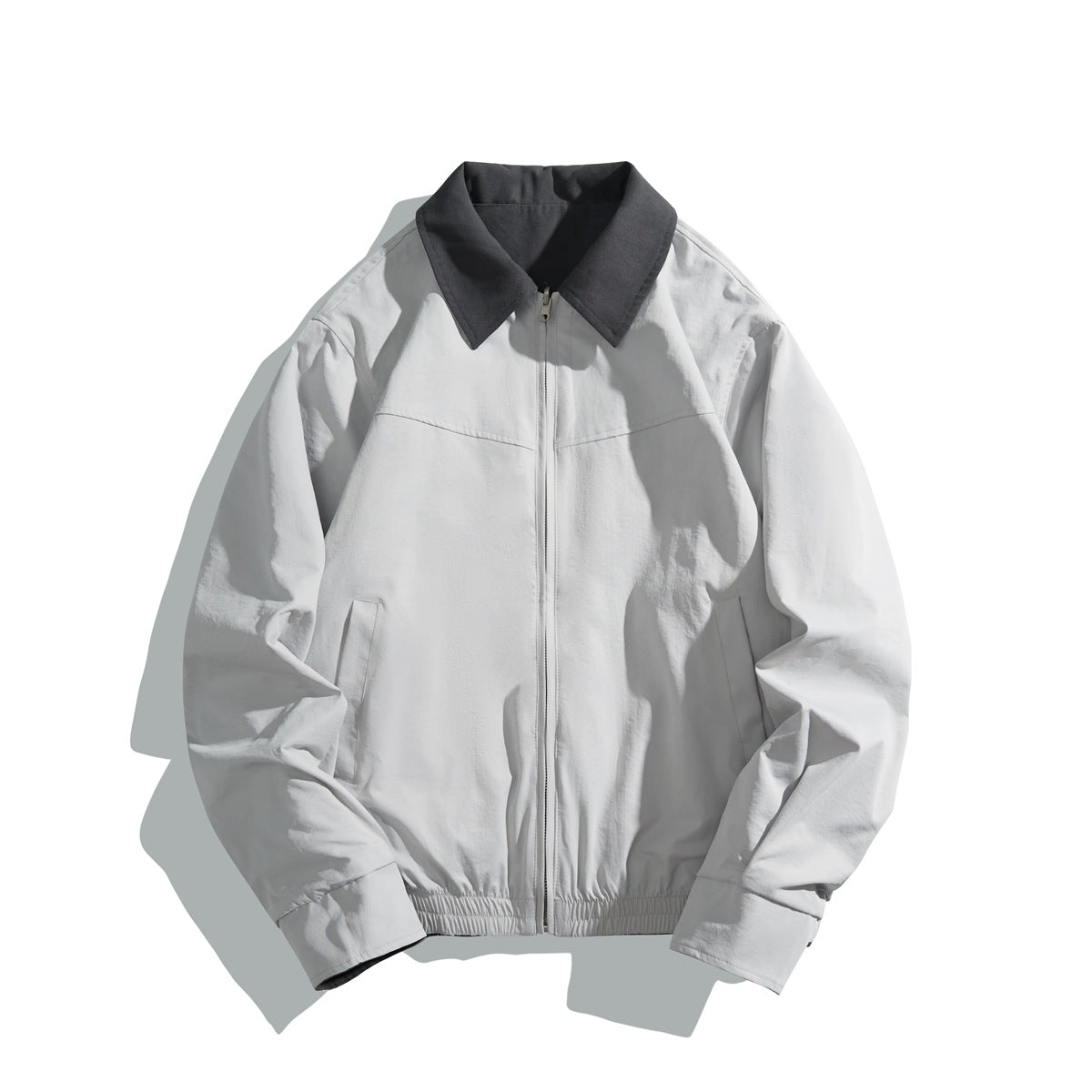 Front view of a light gray zip-front jacket with a charcoal pointed collar, side pockets, and elastic hem.