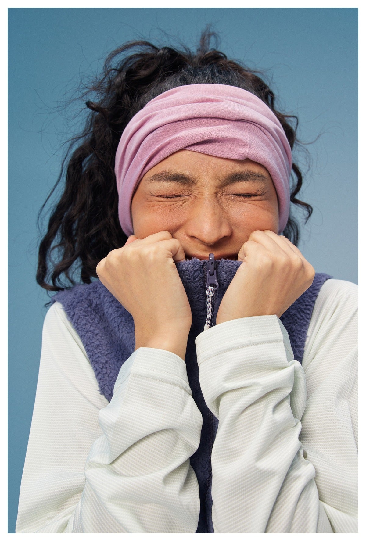 Close-up of a model wearing a purple vest with a front zipper and a pink headband.