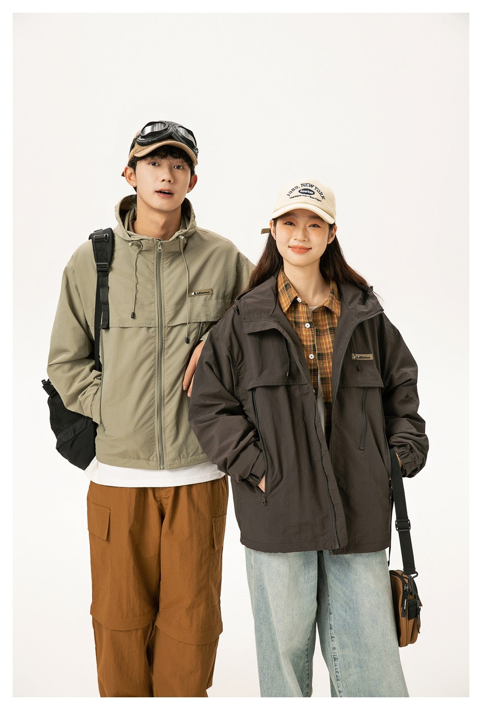 Two models pose together in khaki and dark brown hooded jackets, shown from about mid-thigh up.