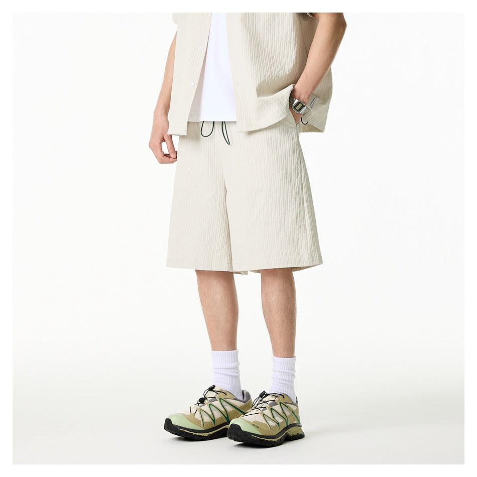 Angled front view of a model wearing ivory drawstring shorts with a matching short-sleeve shirt and white tee.