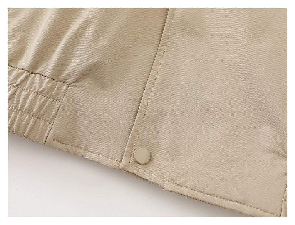 Close-up of a beige jacket's elasticated hem and snap-button front edge.