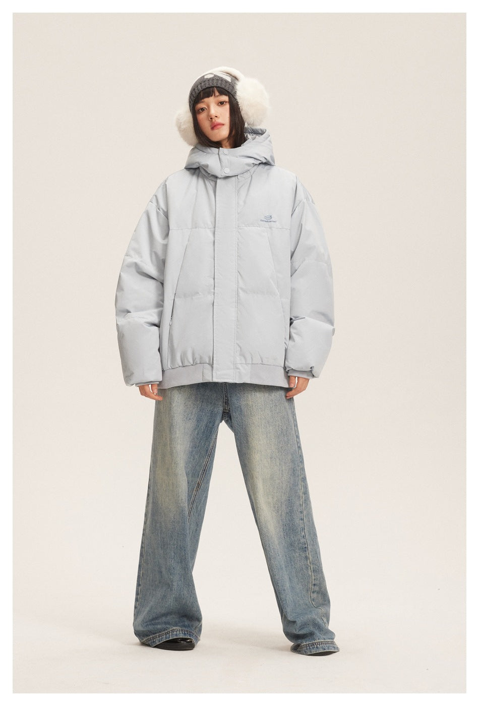 Full-length front view of a model wearing a light gray hooded puffer jacket with wide-leg jeans.