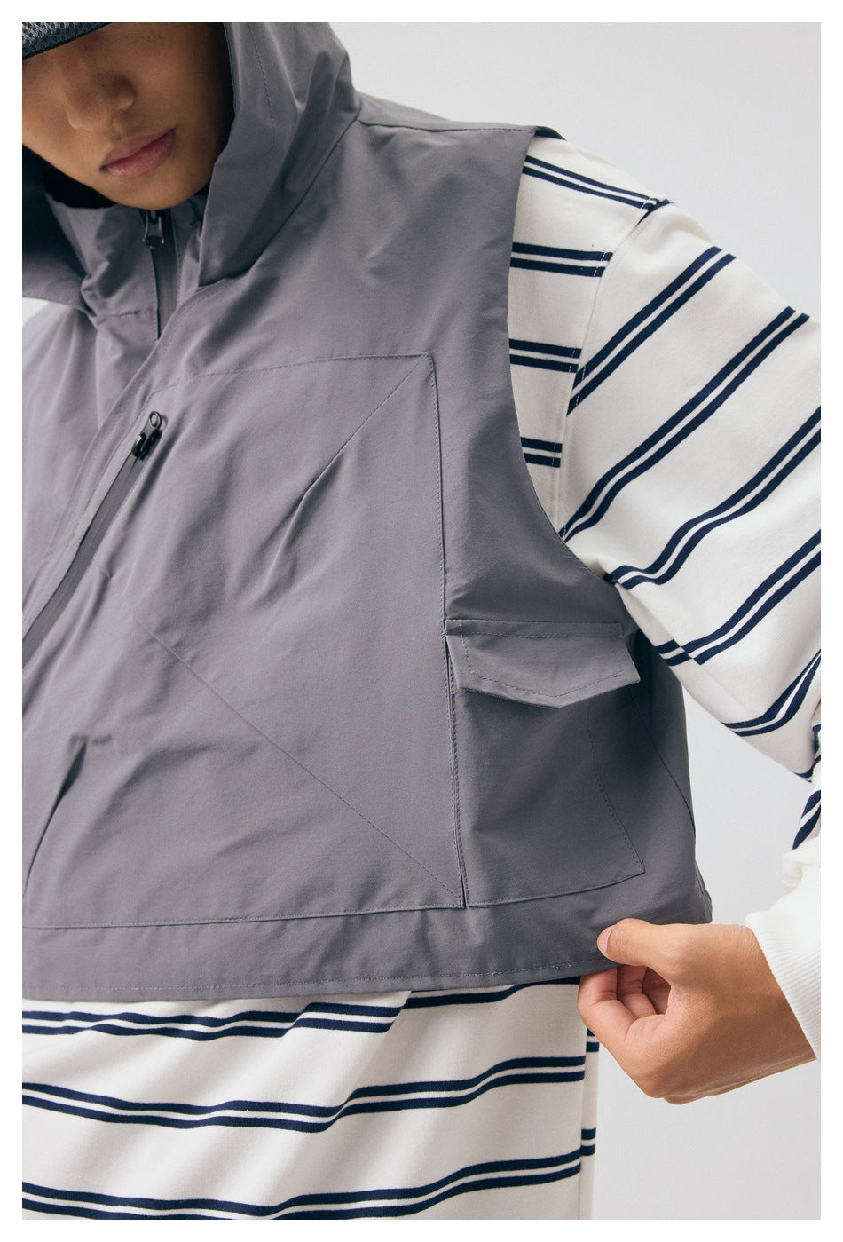 Close-up of the gray vest showing its diagonal chest zipper, large front pocket, and side flap pocket.