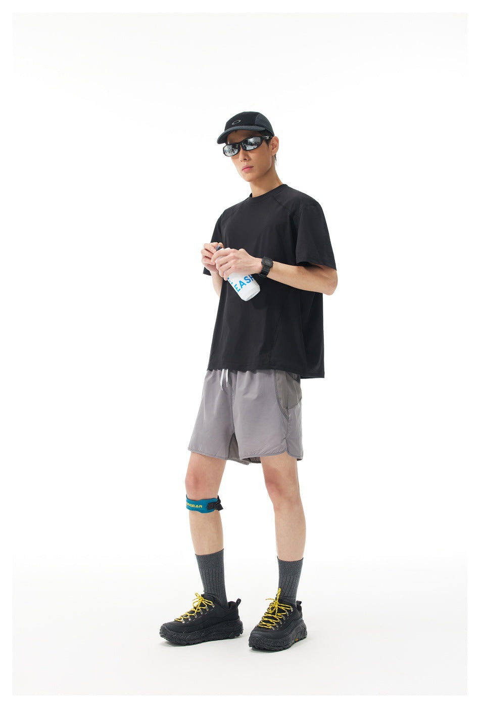 Model wearing a black short-sleeve shirt and gray athletic shorts, shown from the front at an angle.