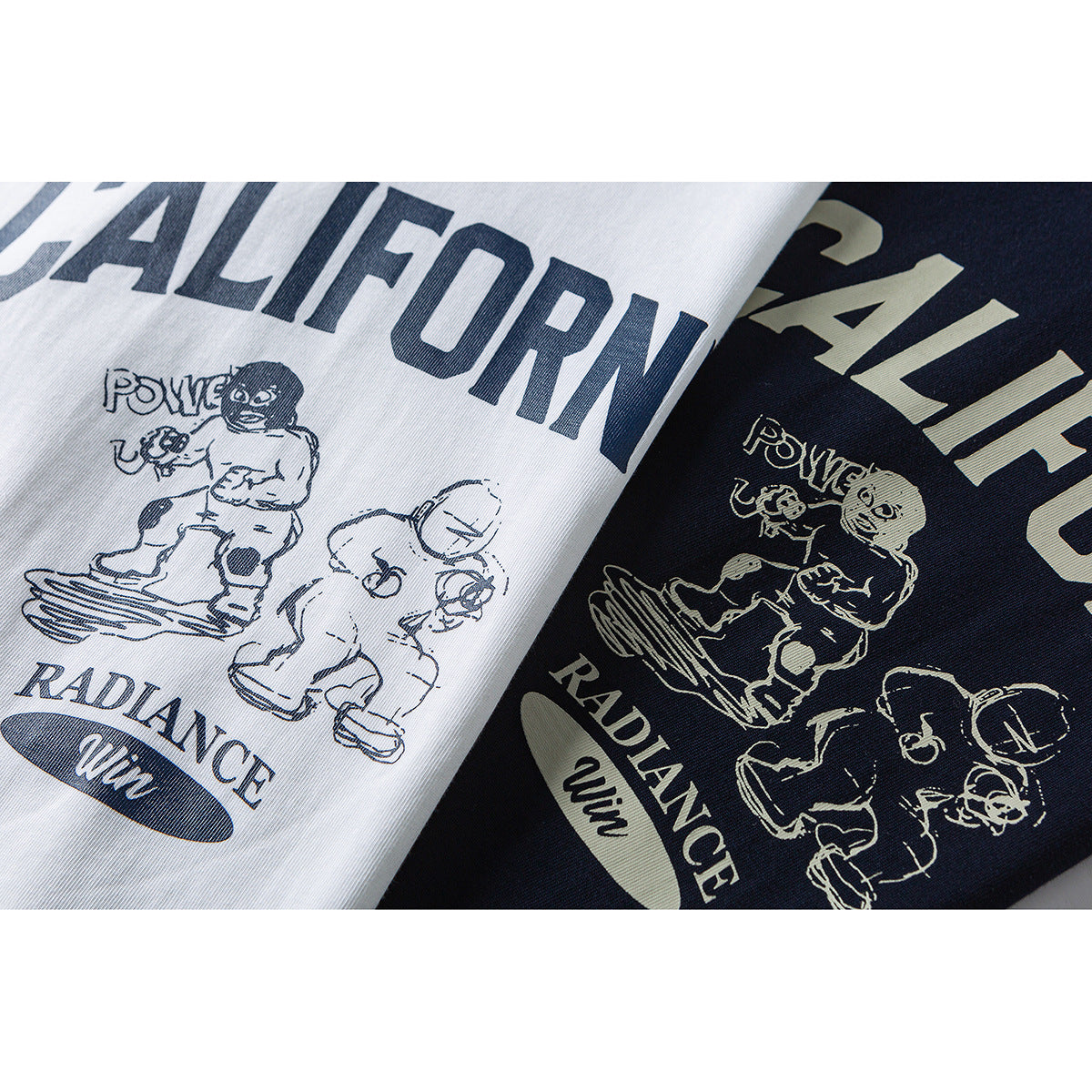 Close-up of white and navy T-shirts with bold lettering and illustrated figures printed on the front.