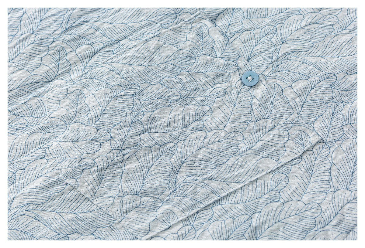 Close-up of a blue button and placket on pale shirt fabric with an allover blue leaf pattern.