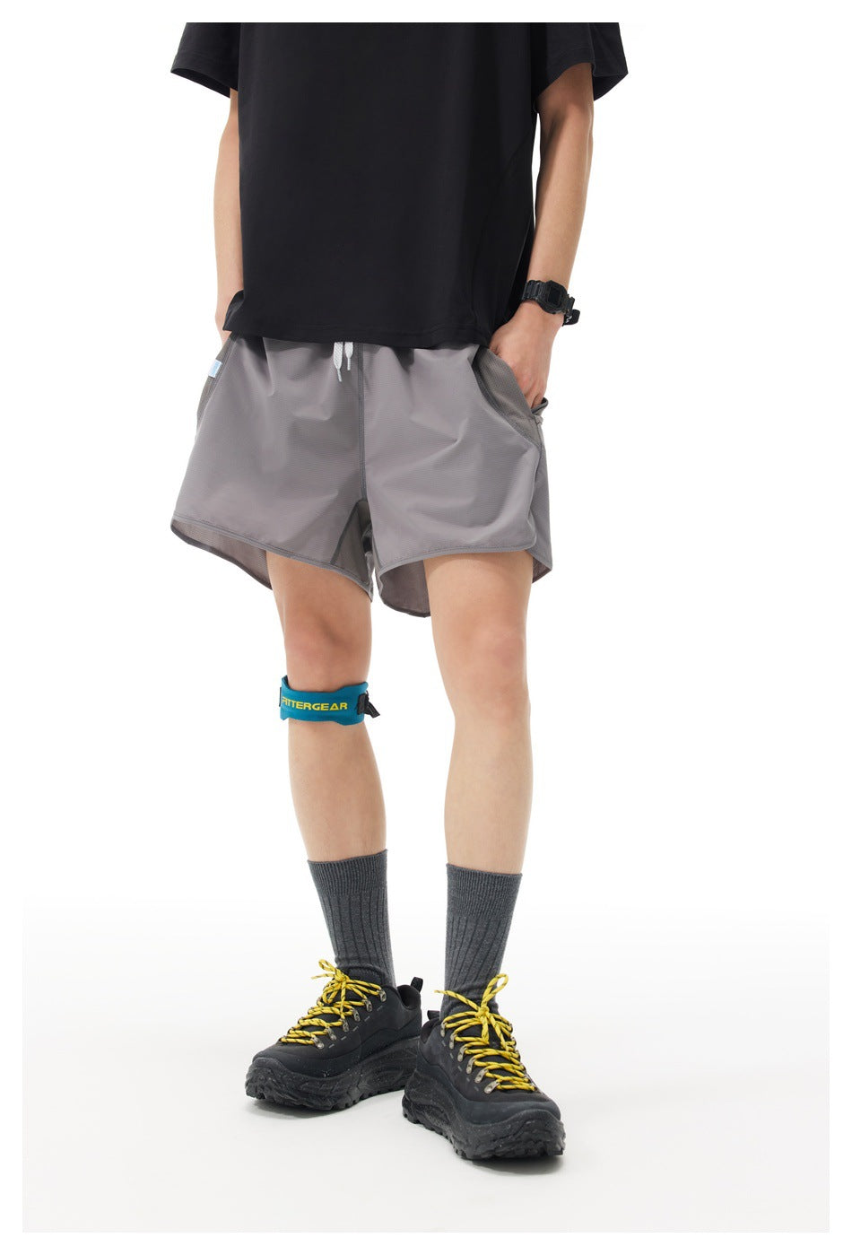 A model stands with hands in the pockets of loose gray drawstring shorts, shown from a slight angle.