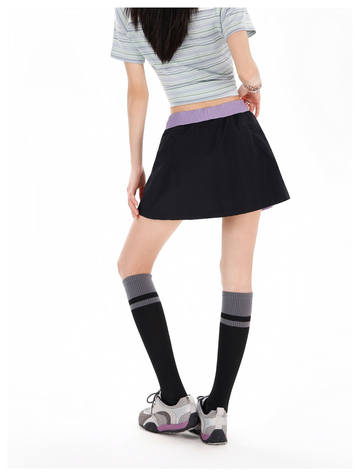 Back view of a model wearing a black flared skirt with a lavender waistband and a striped cropped top.