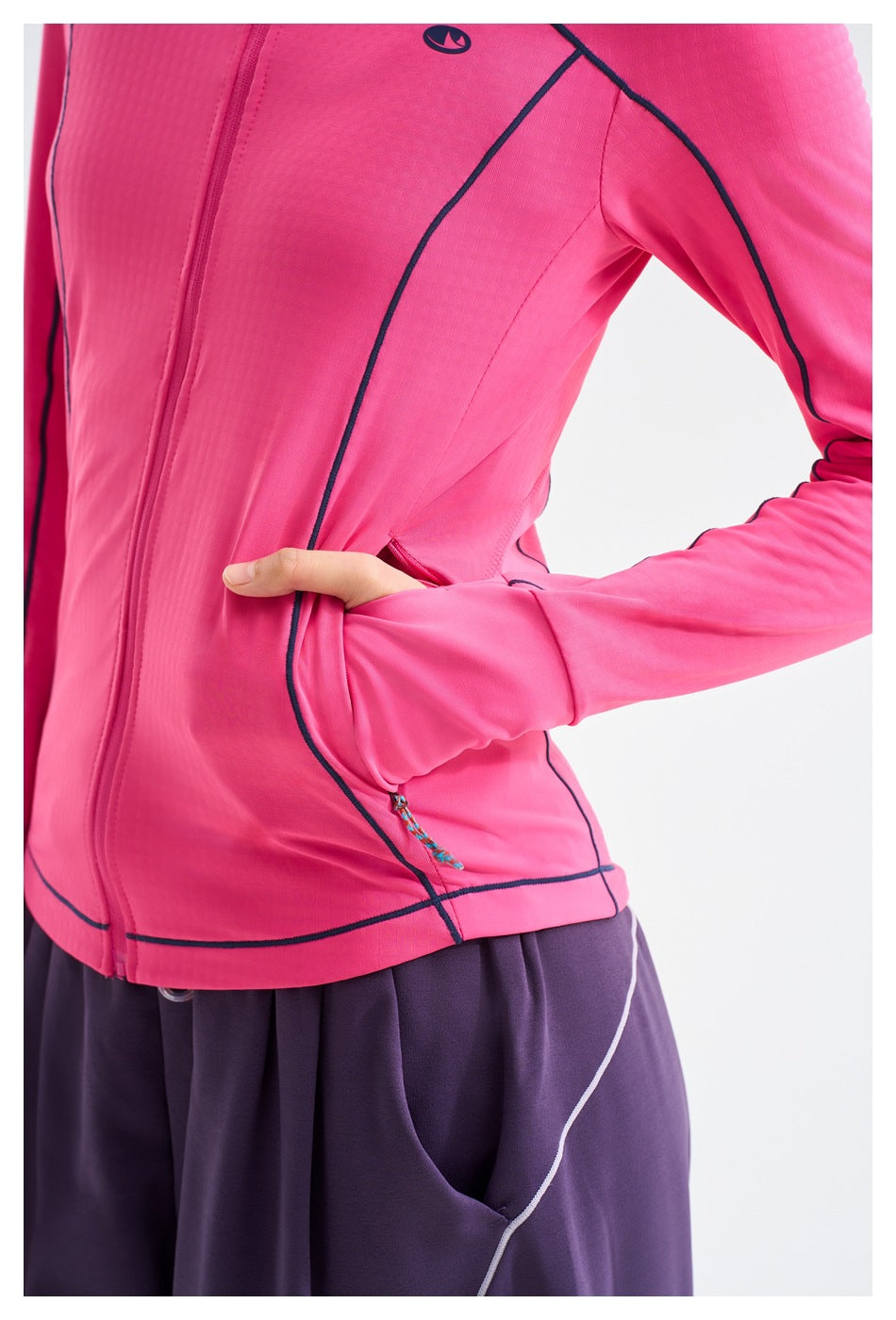Close-up of the pink jacket's side pocket, navy piping, zipper pull, and hem, with purple pants below.