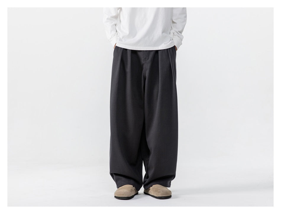 Person wearing dark gray wide-leg pleated trousers with a white long-sleeve top and tan clogs, front view