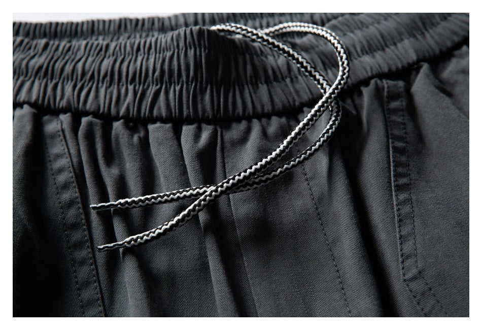 Close-up of dark charcoal pants with a gathered elastic waistband and contrasting braided drawstring.