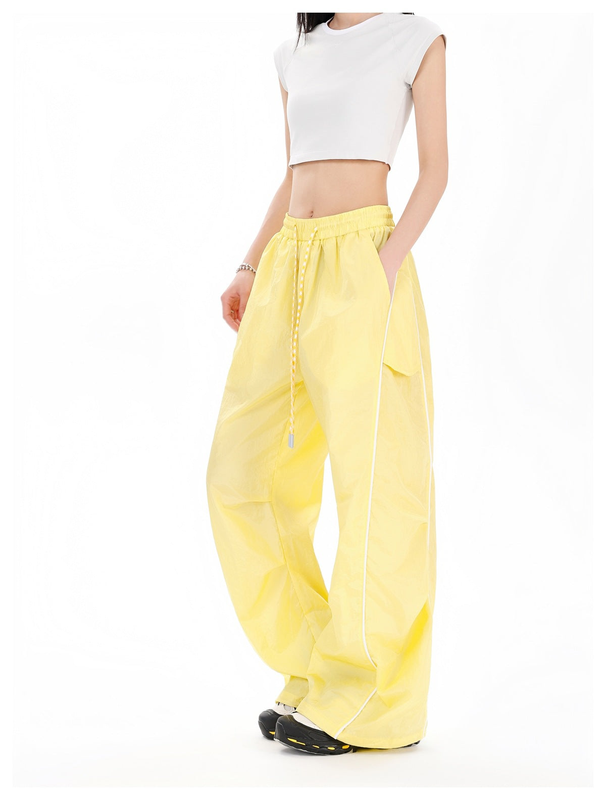 Three-quarter view of a model wearing yellow wide-leg pants with a drawstring waist, side pockets, and white piping.