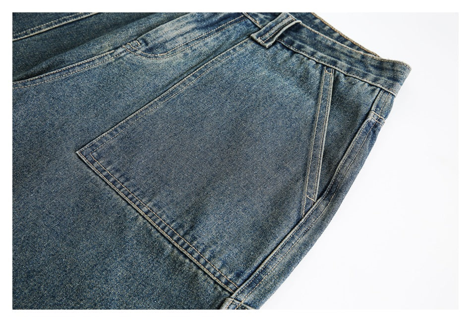 Close-up of a large stitched pocket and side seam on blue washed denim trousers.