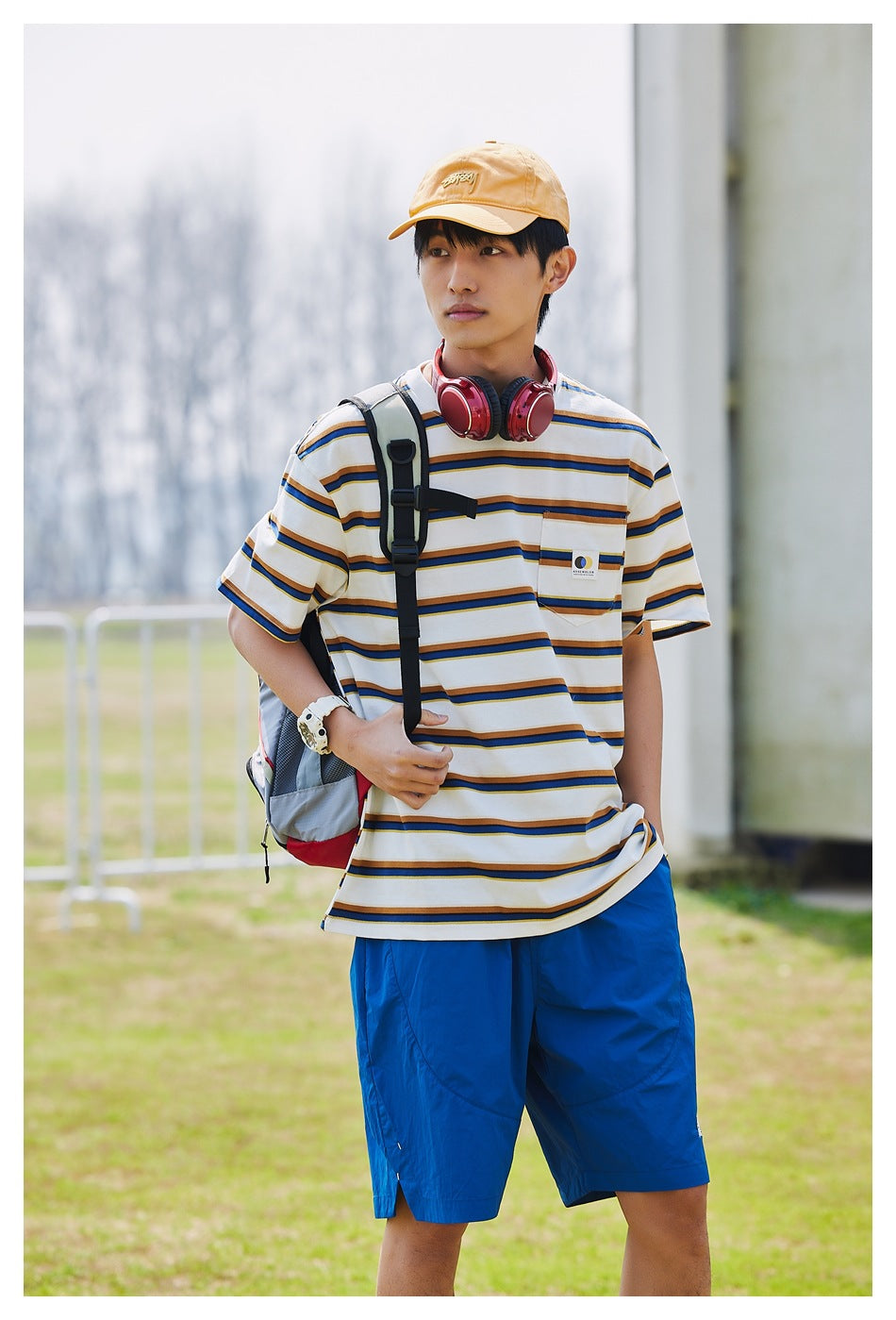 Model wearing a white T-shirt with navy and mustard stripes and bright blue shorts, viewed from the front.