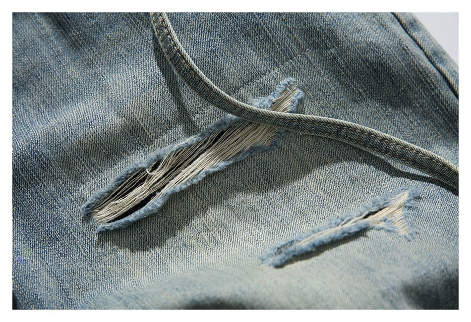 Close-up of faded blue denim with elongated frayed rips and a diagonal seam.