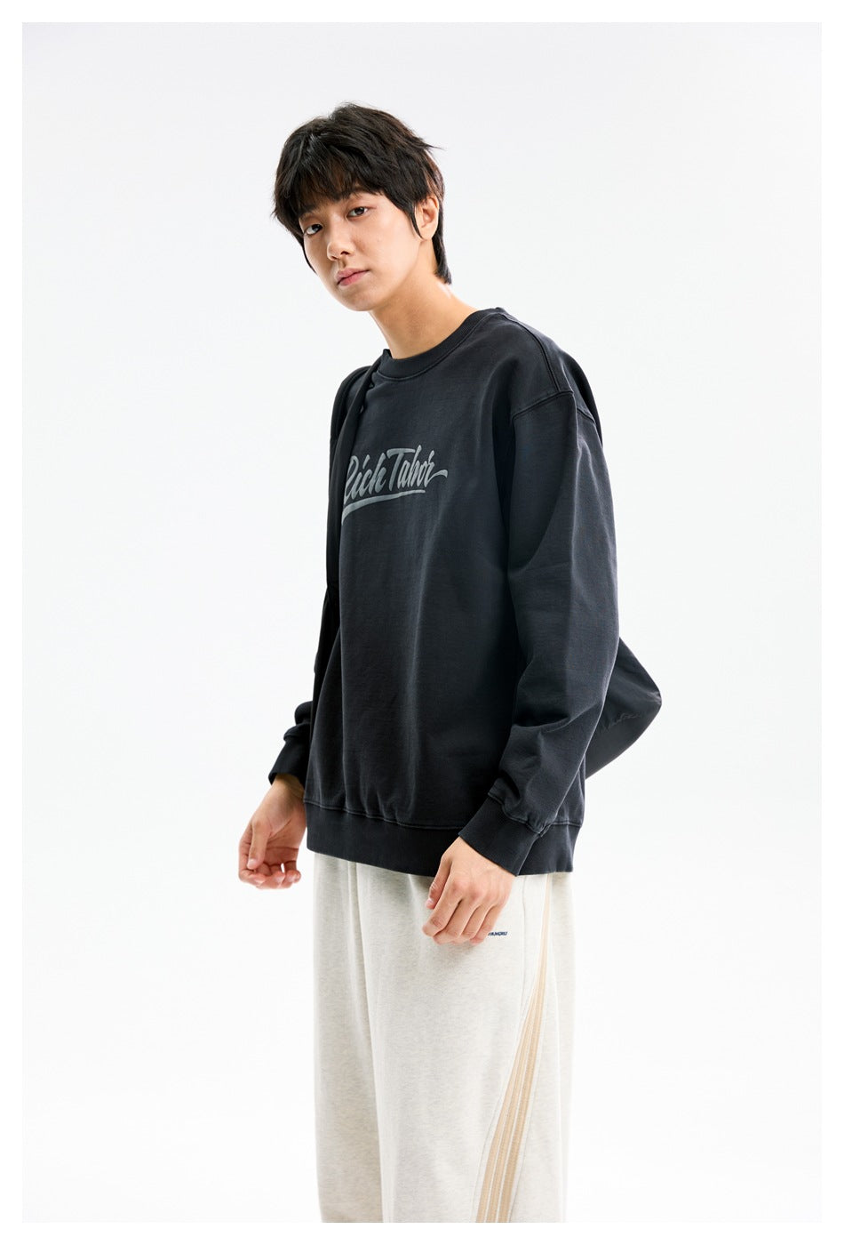 Three-quarter view of a model wearing a black script-print crewneck sweatshirt.