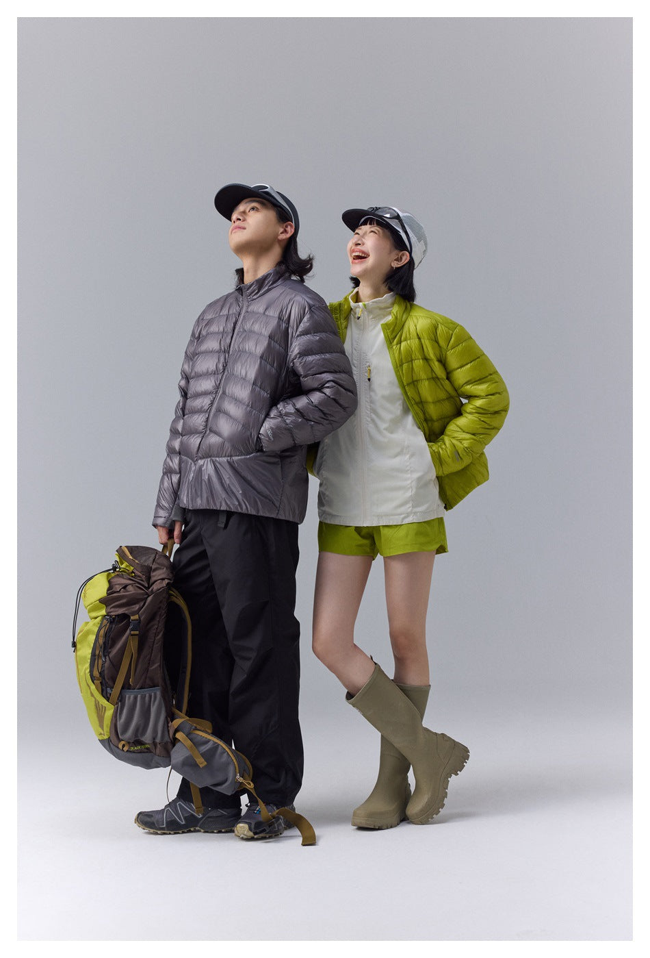 Two models pose in charcoal gray and lime green quilted jackets with outdoor clothing and gear.