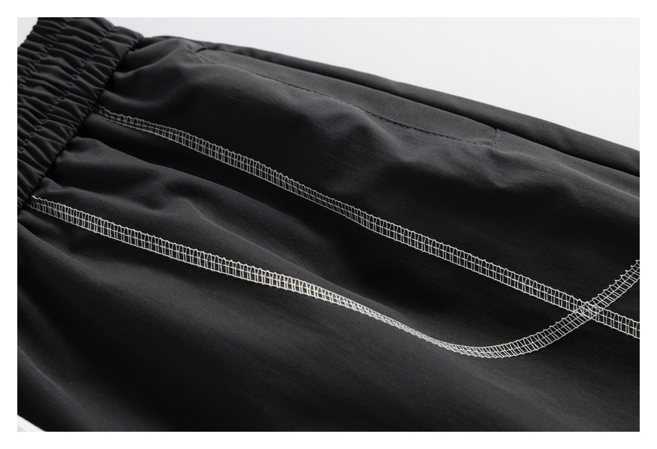 Close-up of black pants with a gathered elastic waistband and two curved rows of contrasting white overlock stitching.