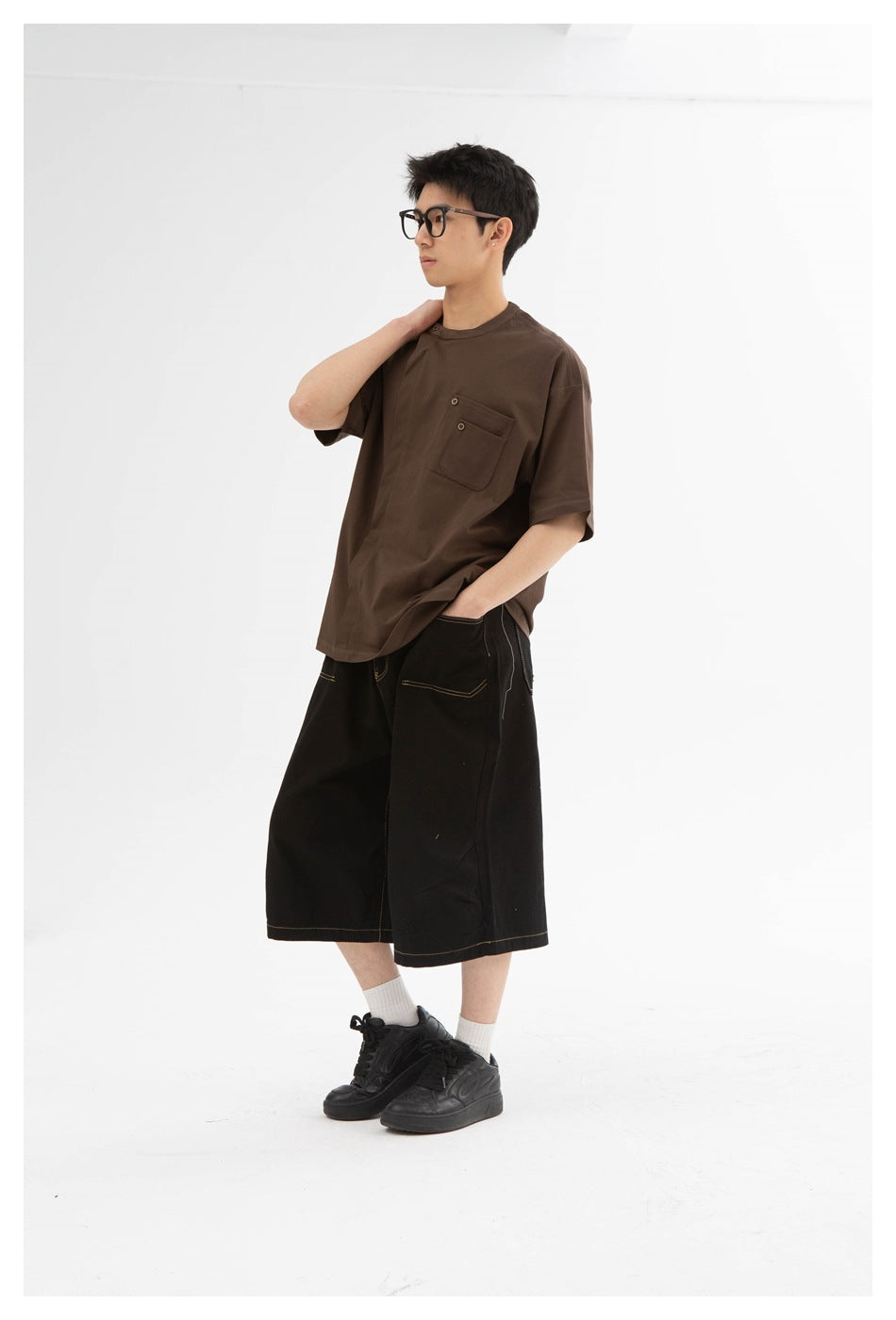 Model wearing an oversized dark brown short-sleeve T-shirt with a button-detailed chest pocket and black wide shorts.