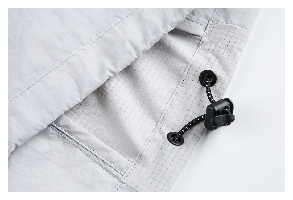 Close-up of a black elastic drawcord and toggle attached to a stitched edge of a light gray garment.