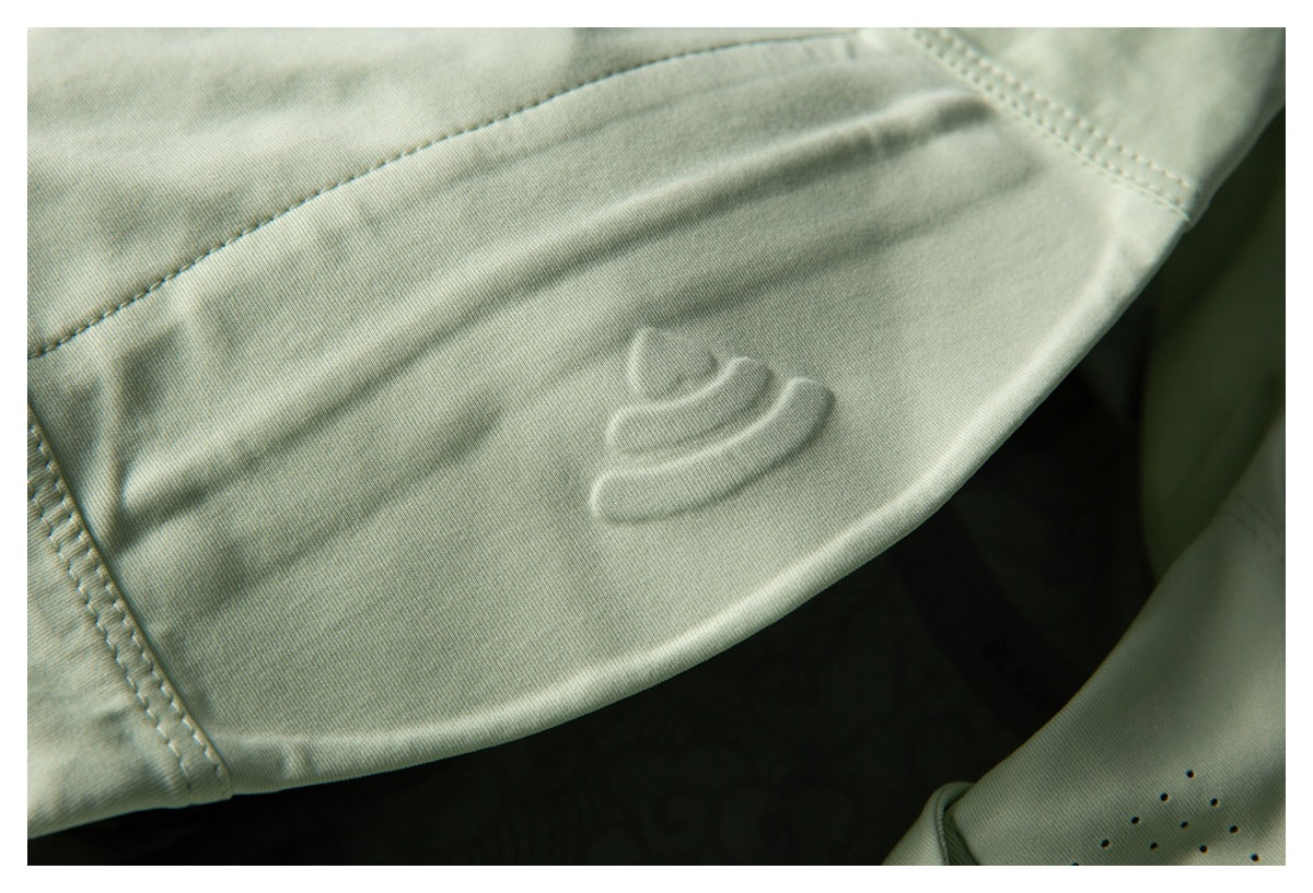 Close-up of a raised emblem on the pale green jacket hood, with stitching and zipper teeth visible at the edge.
