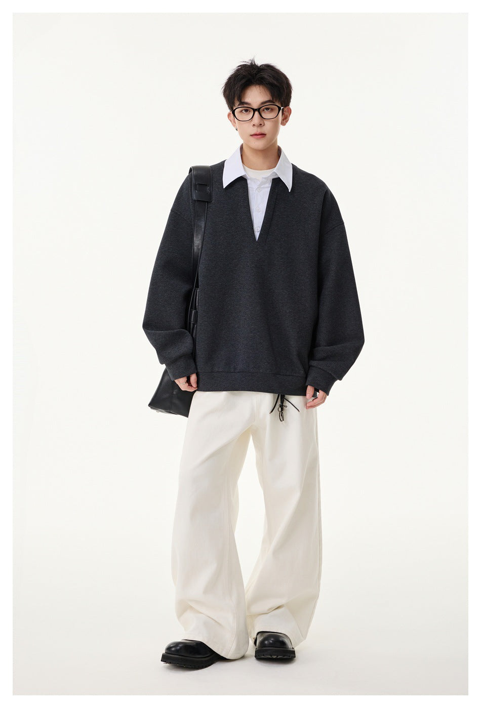 Full-length view of a model wearing a charcoal V-neck pullover over a white collared shirt and loose white trousers.