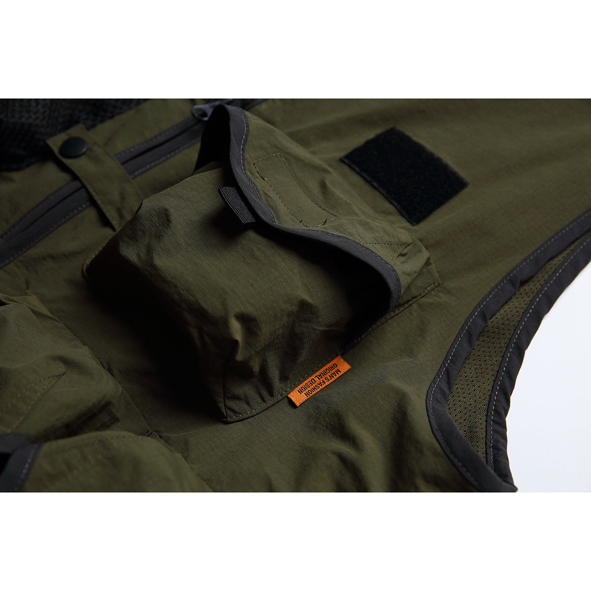 Close-up of an olive vest pocket with a flap, hook-and-loop patch, and black edging.