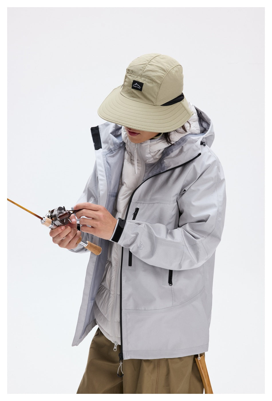 Model in a light gray hooded jacket over a white quilted layer, shown handling a fishing rod.