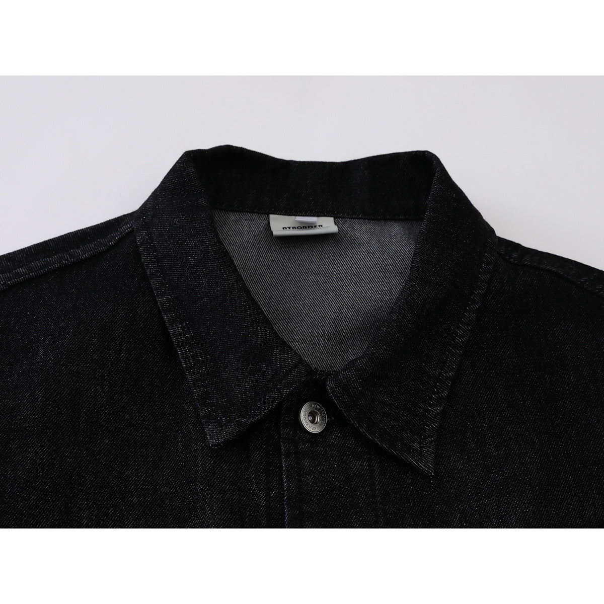Close-up of a black denim jacket collar, inner label and silver button.