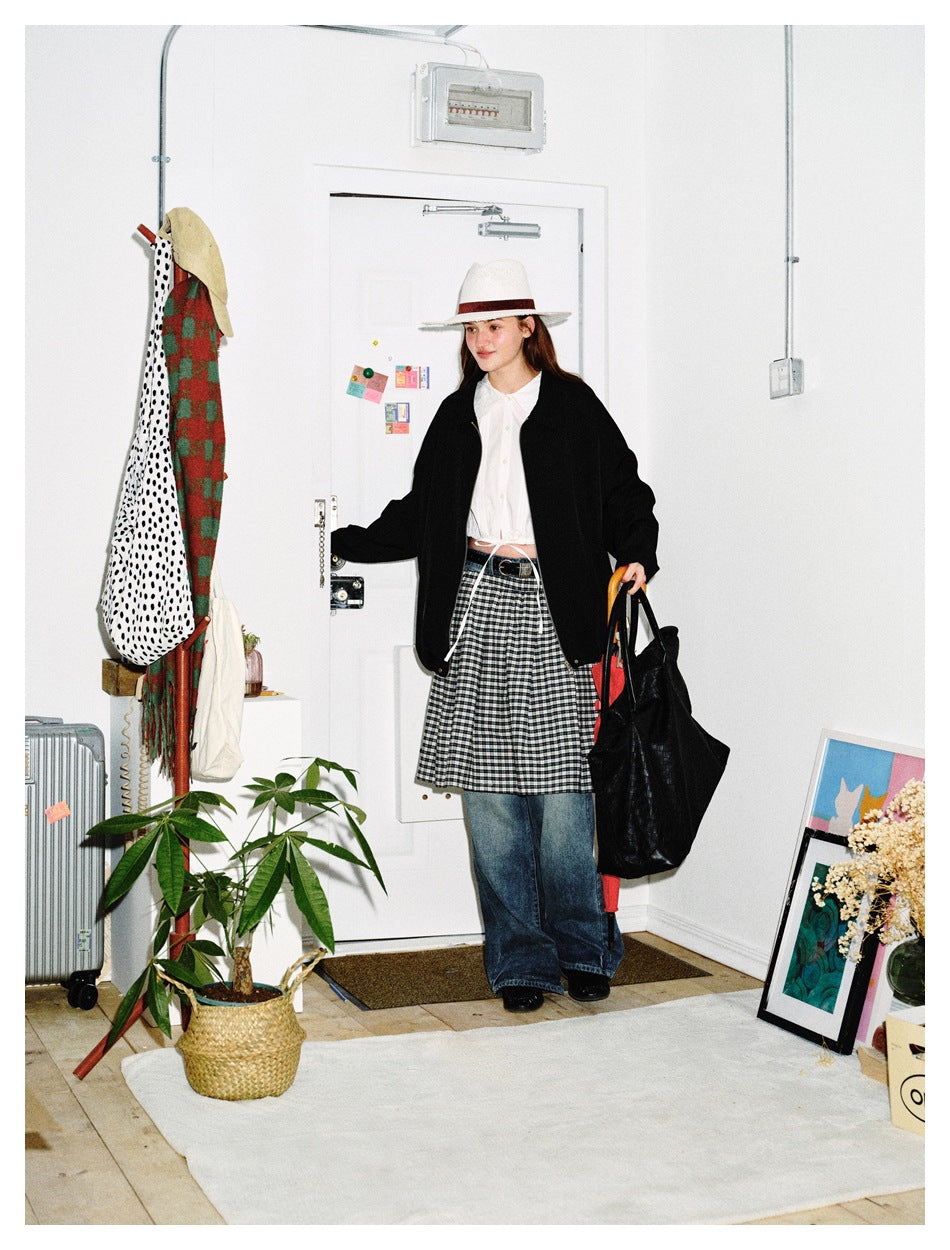 Full-length model in a black jacket, white blouse, checked skirt over blue jeans, and white hat.