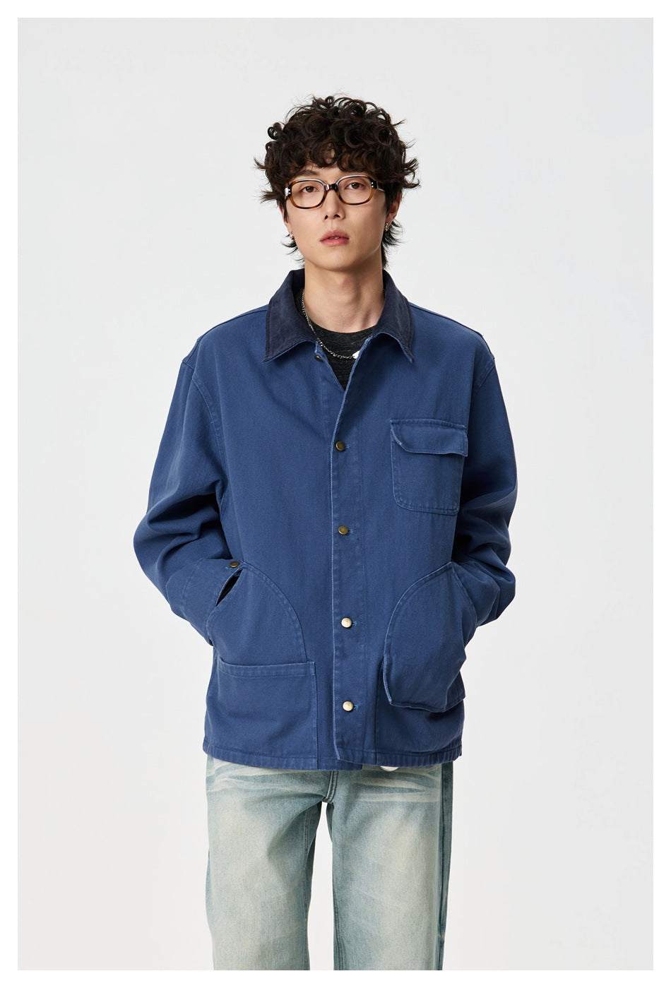 Model with hands in pockets wearing a blue snap-front chore jacket with navy collar and light washed jeans