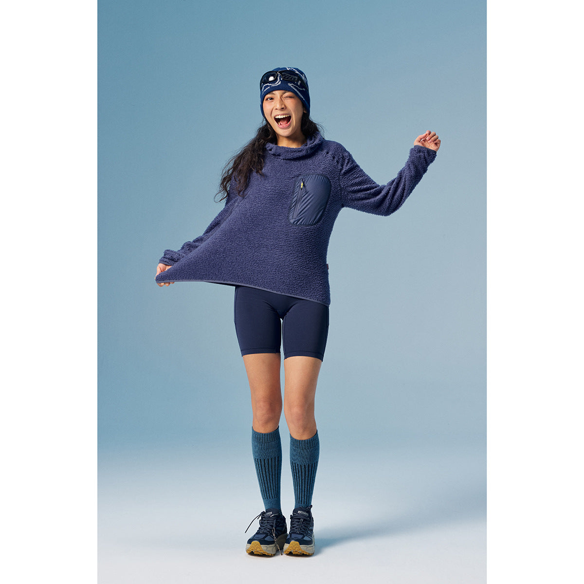 Full-length front view of a model in a navy textured pullover with a chest pocket, navy shorts and tall socks.