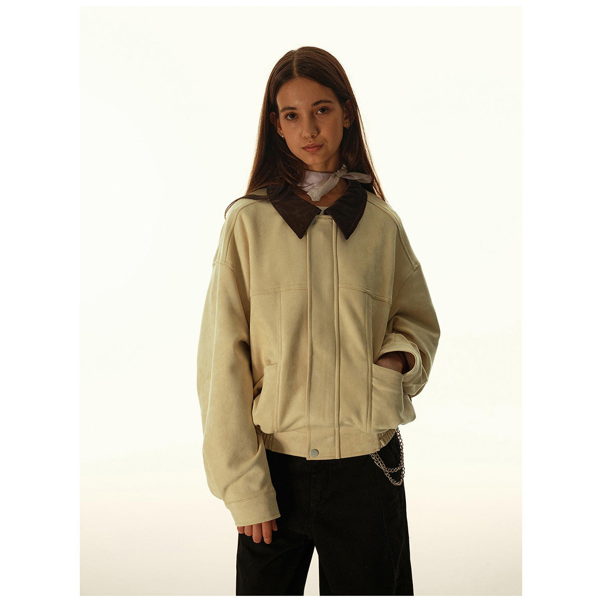 Woman wearing a cropped beige jacket with a dark pointed collar, front pockets, and a snap-button hem.