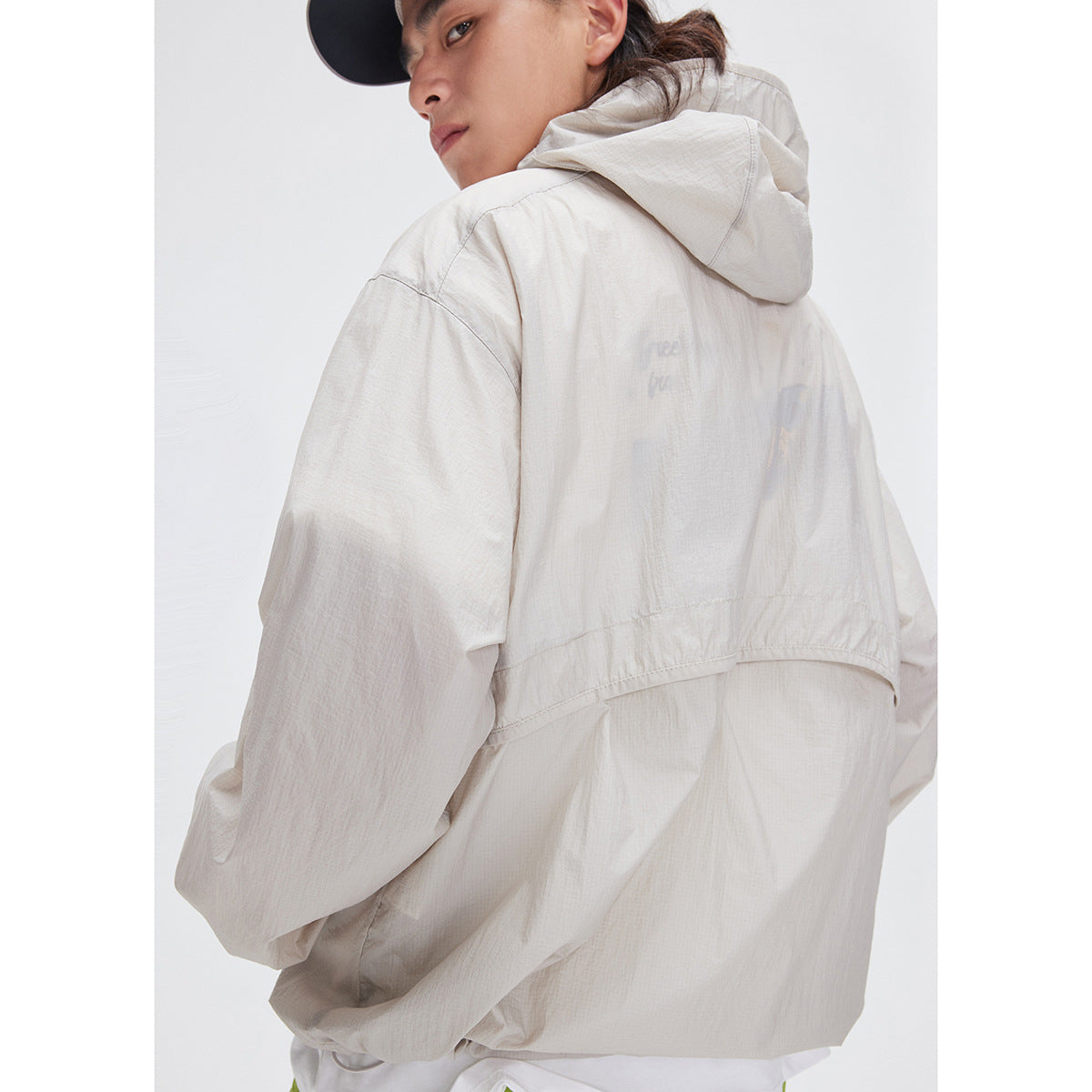 Close rear view of a model wearing a light beige hooded jacket with a curved back seam.