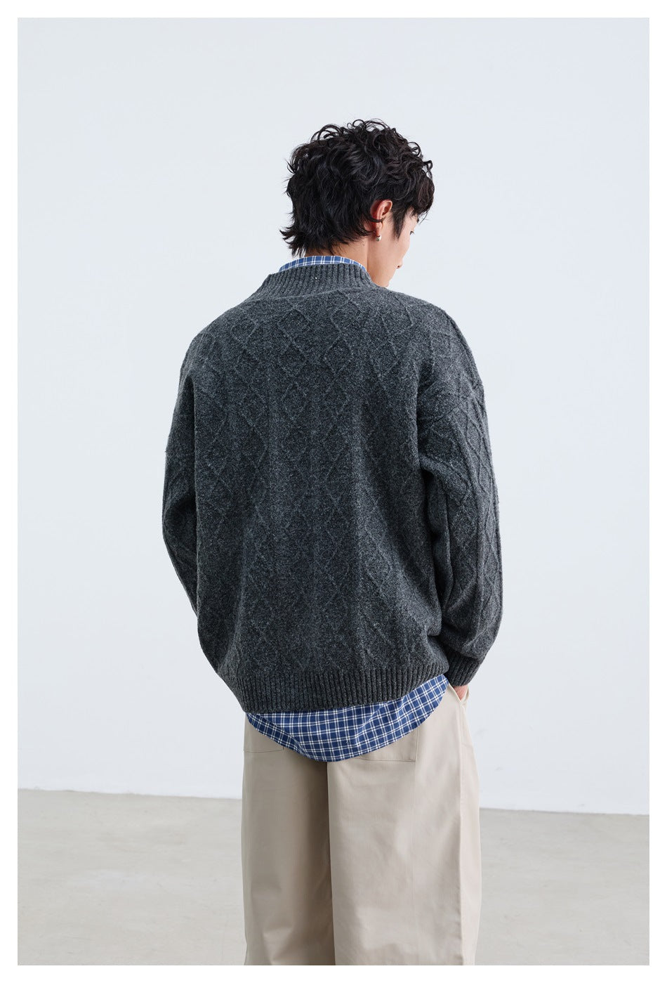 Back view of a model wearing a dark charcoal cable-knit cardigan with ribbed hem and cuffs.