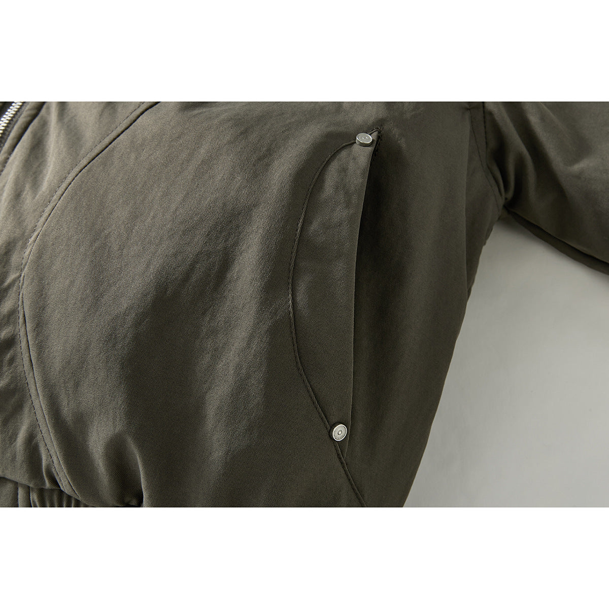 Close-up of an olive-gray jacket's curved side pocket with two small metal snaps.
