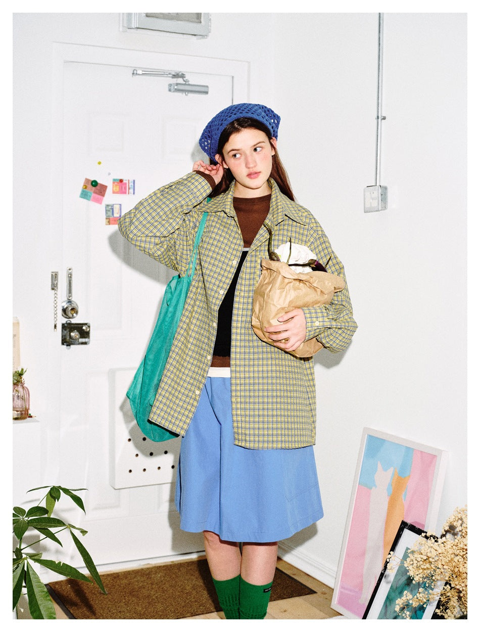 Full-length model wearing a yellow and blue plaid shirt, brown top, blue skirt, and blue knit hat.