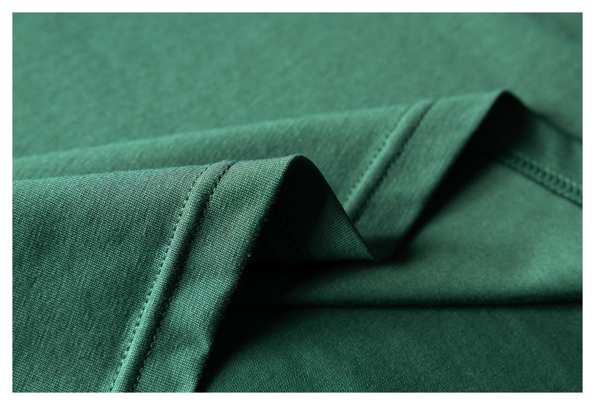 Macro view of dark green T-shirt fabric, folded hem, and stitching.