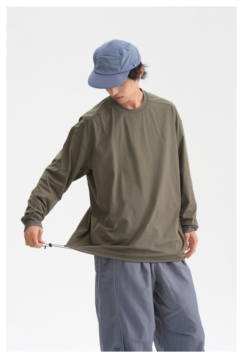 Model showing the fit and adjustable drawcord hem of an olive long-sleeve shirt with slate-blue pants.