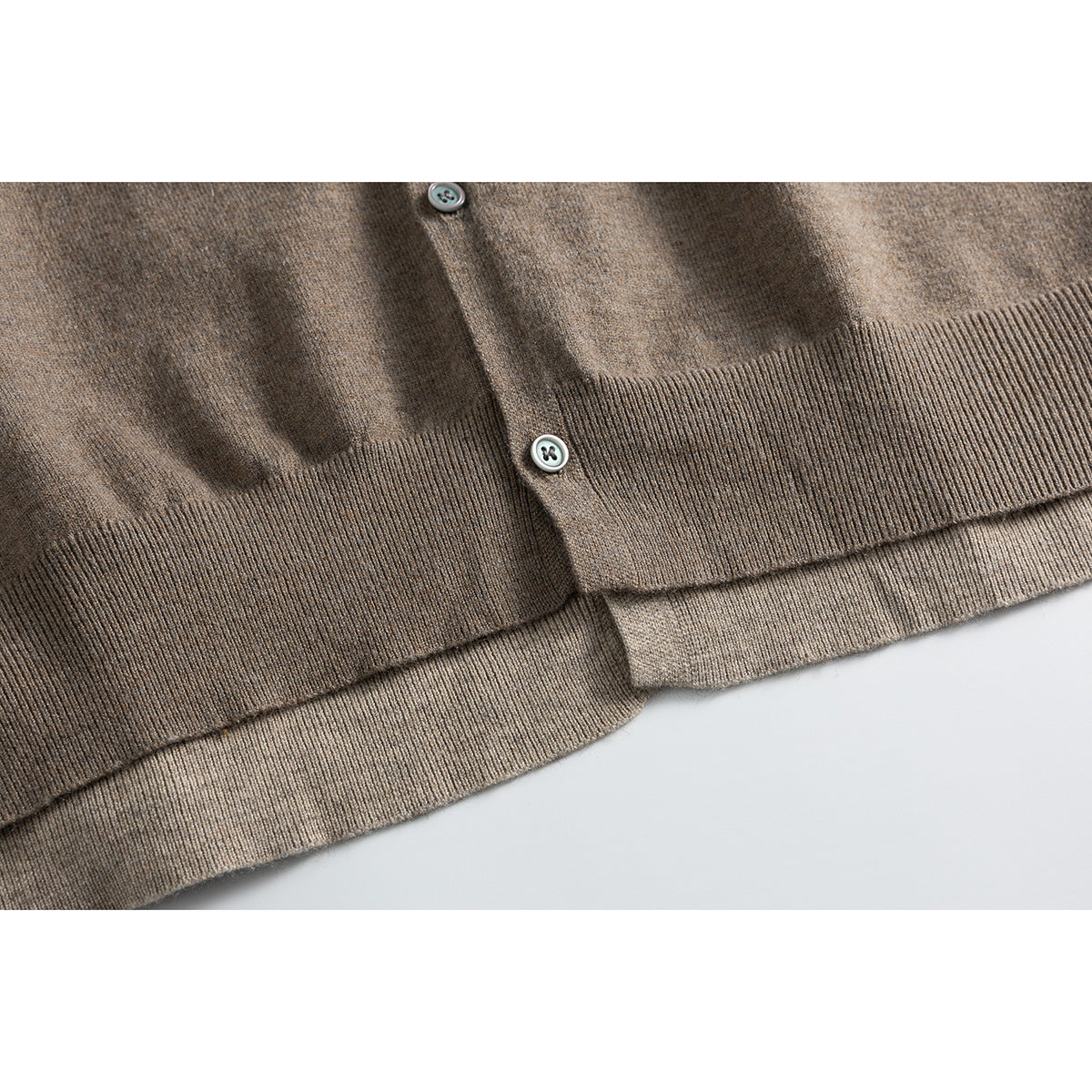 Close-up of the taupe-brown cardigan's button placket, ribbed hem, and layered edge.