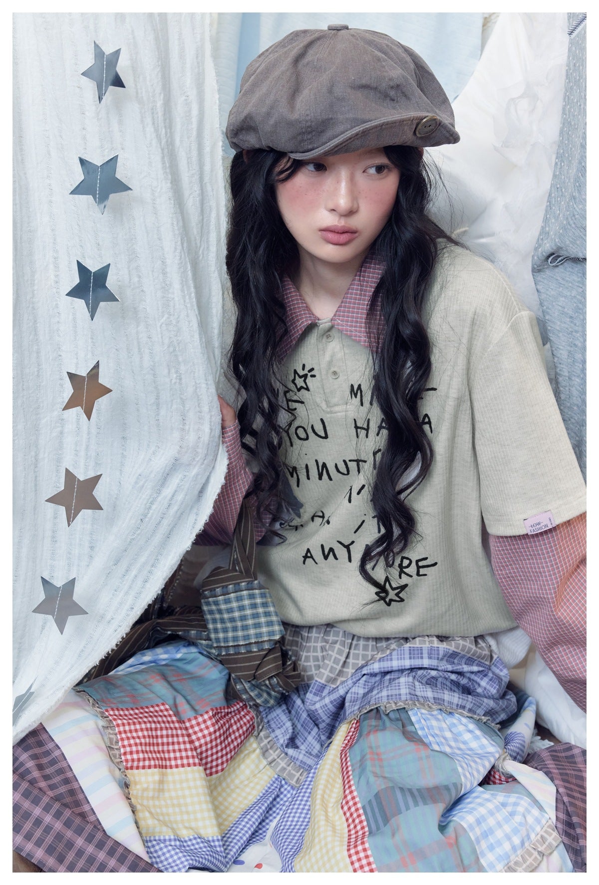 Close view of a model wearing a cream graphic top with red checked layered sleeves and a colorful patchwork skirt.
