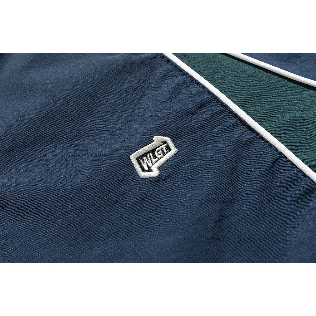 Close-up of a white embroidered patch and piping on navy jacket fabric, with a dark green panel.