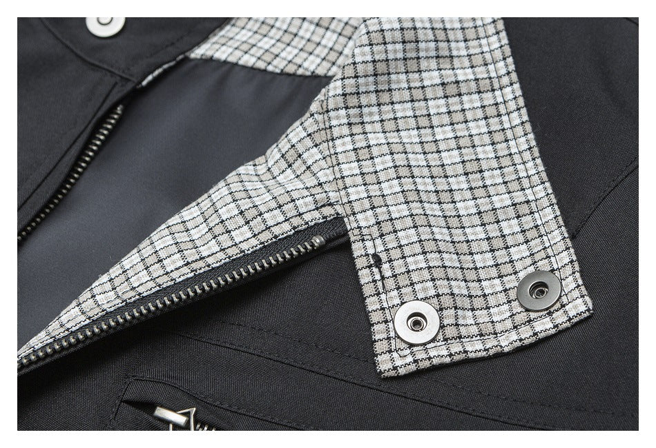 Close-up of a black garment with a gray checked panel, metal zipper, and snap fasteners.
