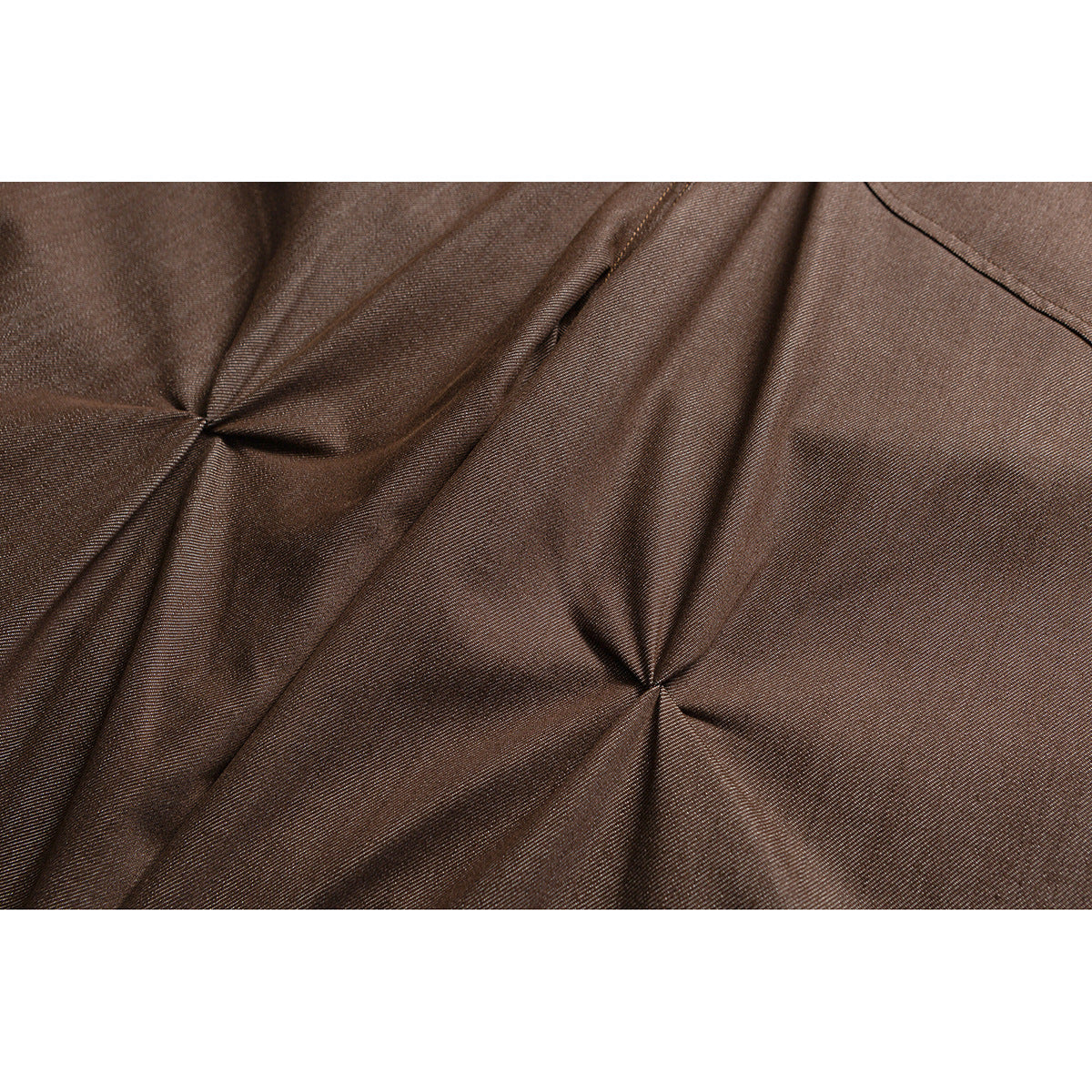 Close-up of brown trouser fabric with stitched seams and gathered folds.