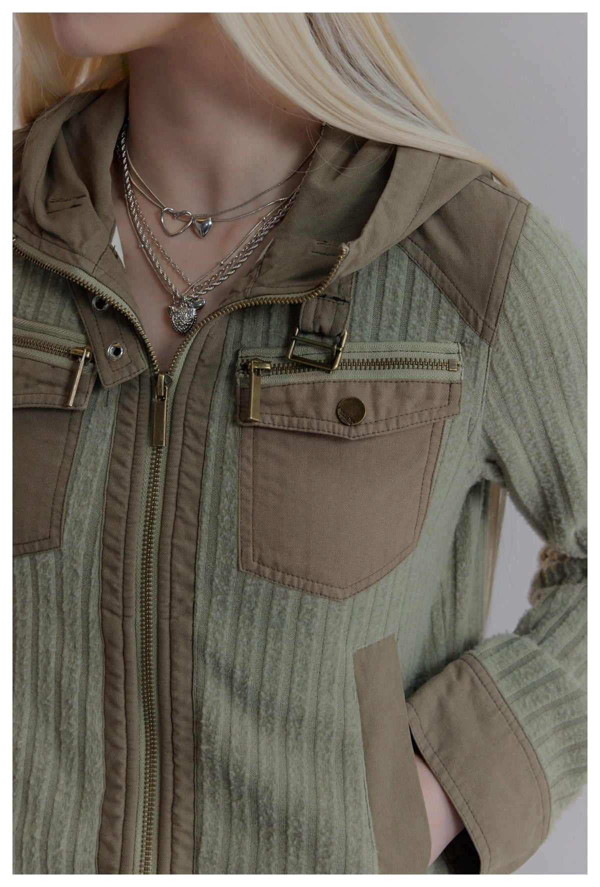 Close-up of a model wearing the jacket, showing its ribbed fabric, taupe chest pockets, hood and brass-tone zippers.
