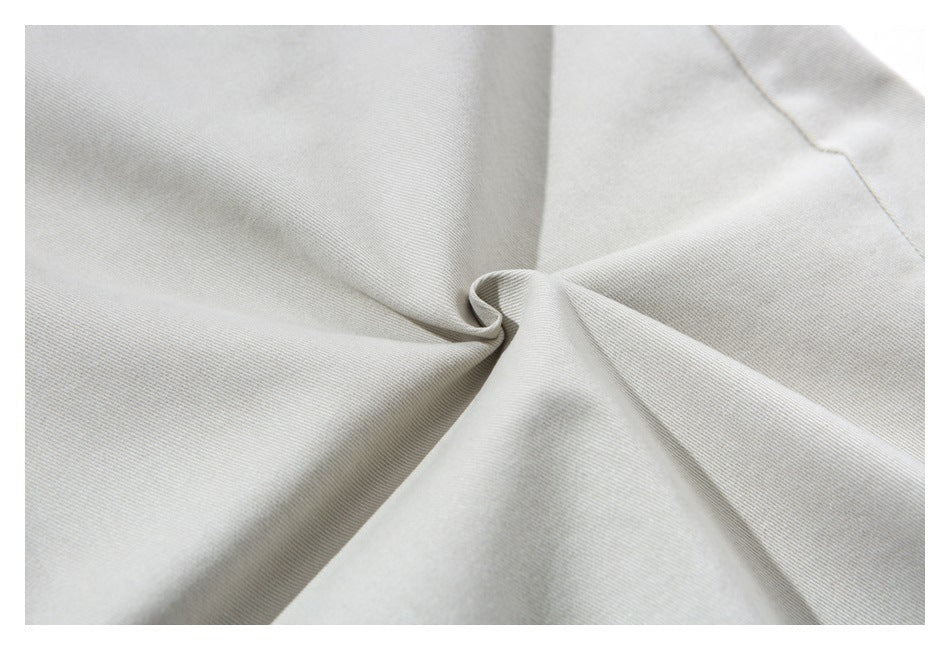 Close-up of light beige trouser fabric gathered into a twist, showing its fine diagonal weave.
